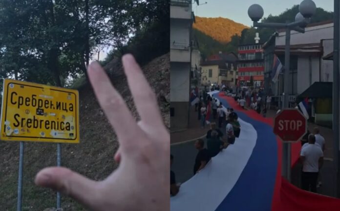 Fotografija osobe ispred saobraćajnog znaka Srebrenica uz podignuta tri prsta